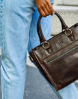 Person holding a brown leather handbag on a street