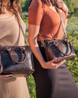 Two women holding brown handbags in a field with greenery | Bastille M