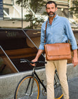 Man holding a brown leather bag next to a bicycle in an urban setting