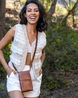 Woman wearing a white crochet vest and white shorts, standing outdoors with greenery in the background.