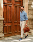 Man holding a brown leather briefcase in front of a large wooden door.