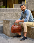 Man sitting on steps holding a brown leather bag in an urban setting
