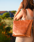 Woman holding a brown leather tote bag with a blurred outdoor background