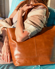 Person sitting on a blue chair holding a brown leather tote bag