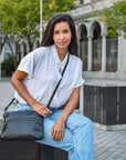 Woman sitting outdoors holding a black handbag, wearing a white shirt and blue jeans.