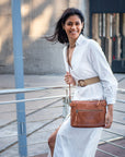 Woman in a white outfit holding a brown leather bag outdoors.