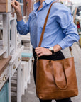 Person holding a brown leather tote bag in an outdoor setting