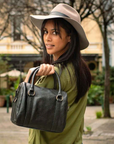 Woman holding a black handbag outdoors with trees and buildings in the background