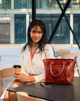Woman sitting at a table with a red handbag and a coffee cup in an outdoor setting.