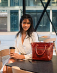 Woman sitting at a table with a red handbag and a coffee cup in an outdoor setting.
