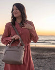 Woman holding a beige handbag on a beach at sunset