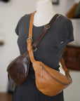 Brown leather crossbody bag on a mannequin with a blurred indoor background