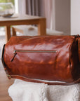 Brown leather duffel bag on a white surface with a blurred indoor background