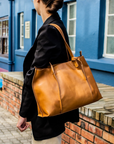 Person holding a brown leather bag in front of a blue building