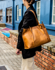 Person holding a brown leather bag in front of a blue building