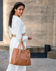 Woman in a white outfit holding a brown leather bag against a stone building background