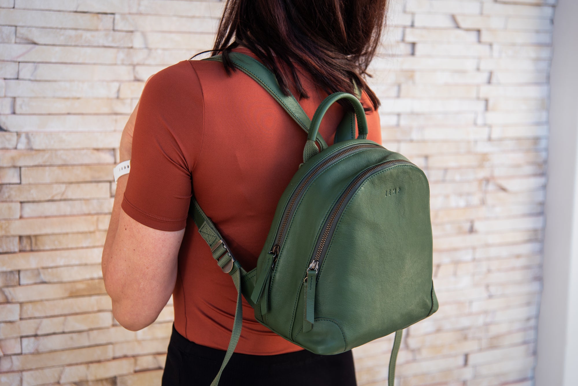 Person wearing a green backpack against a stone wall background