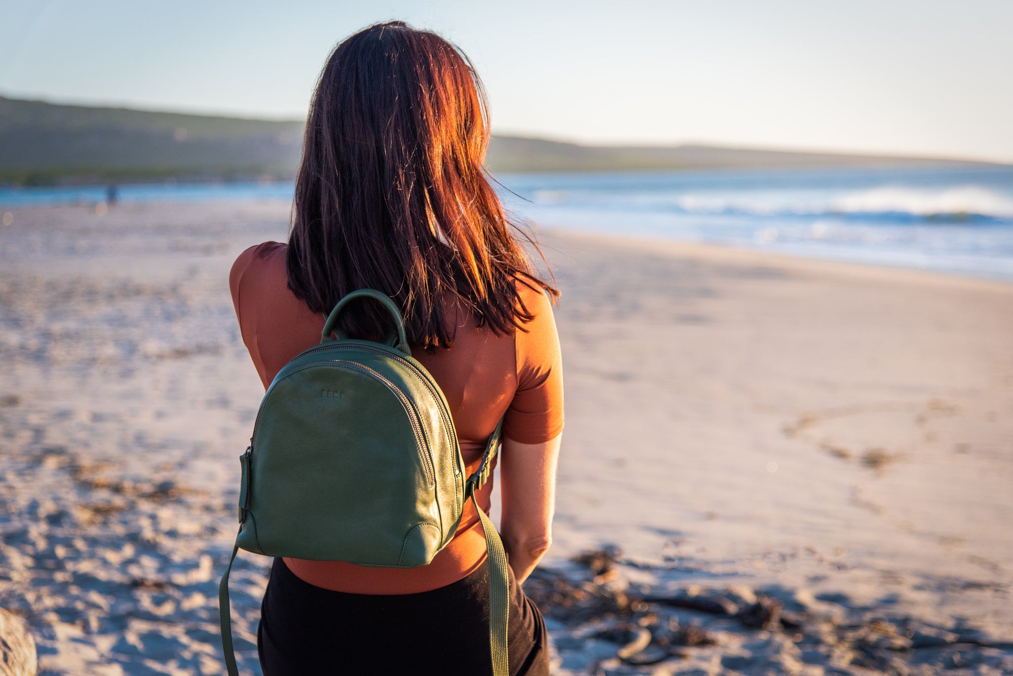 Person with a green backpack standing on a beach