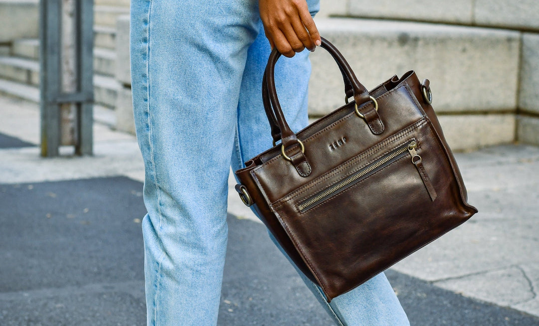 Person holding a brown leather handbag on a street