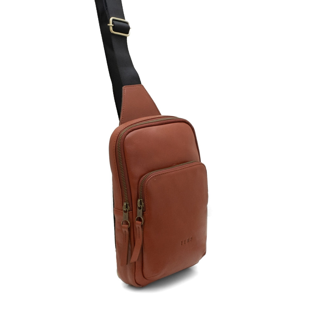 Brown leather sling bag with a black strap on a white background