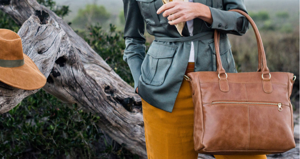 Person holding a brown leather bag with a scenic background