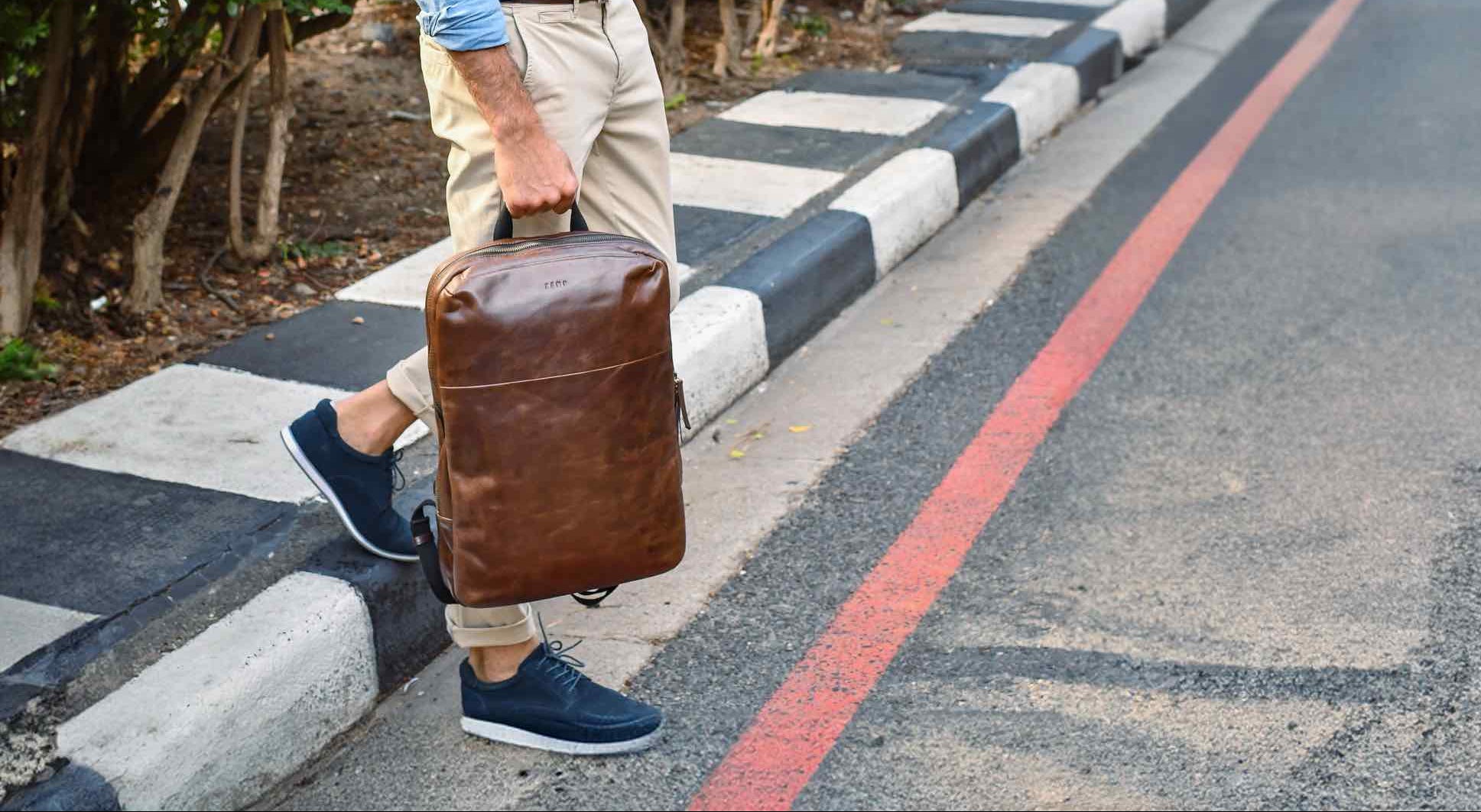 Person holding a brown leather backpack on a zebra crossing