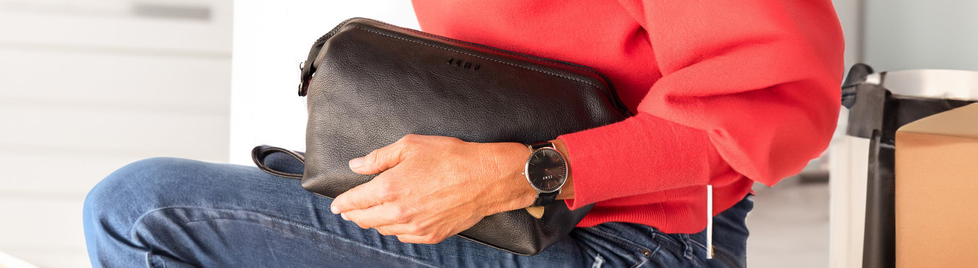 Person holding a leather bag with a watch, sitting on a bench.