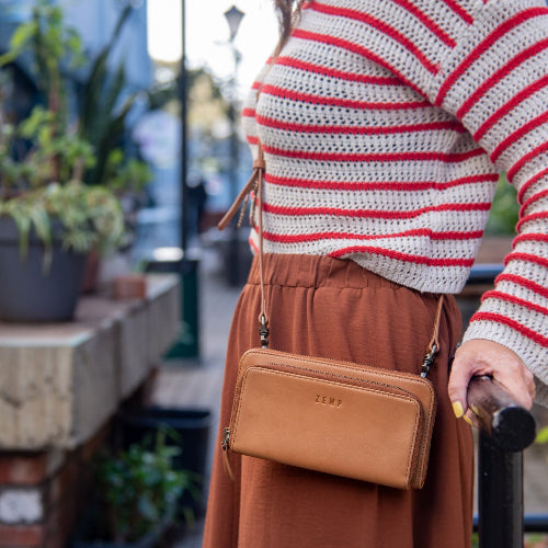 Person wearing a striped sweater and brown skirt with a tan crossbody bag in an outdoor setting