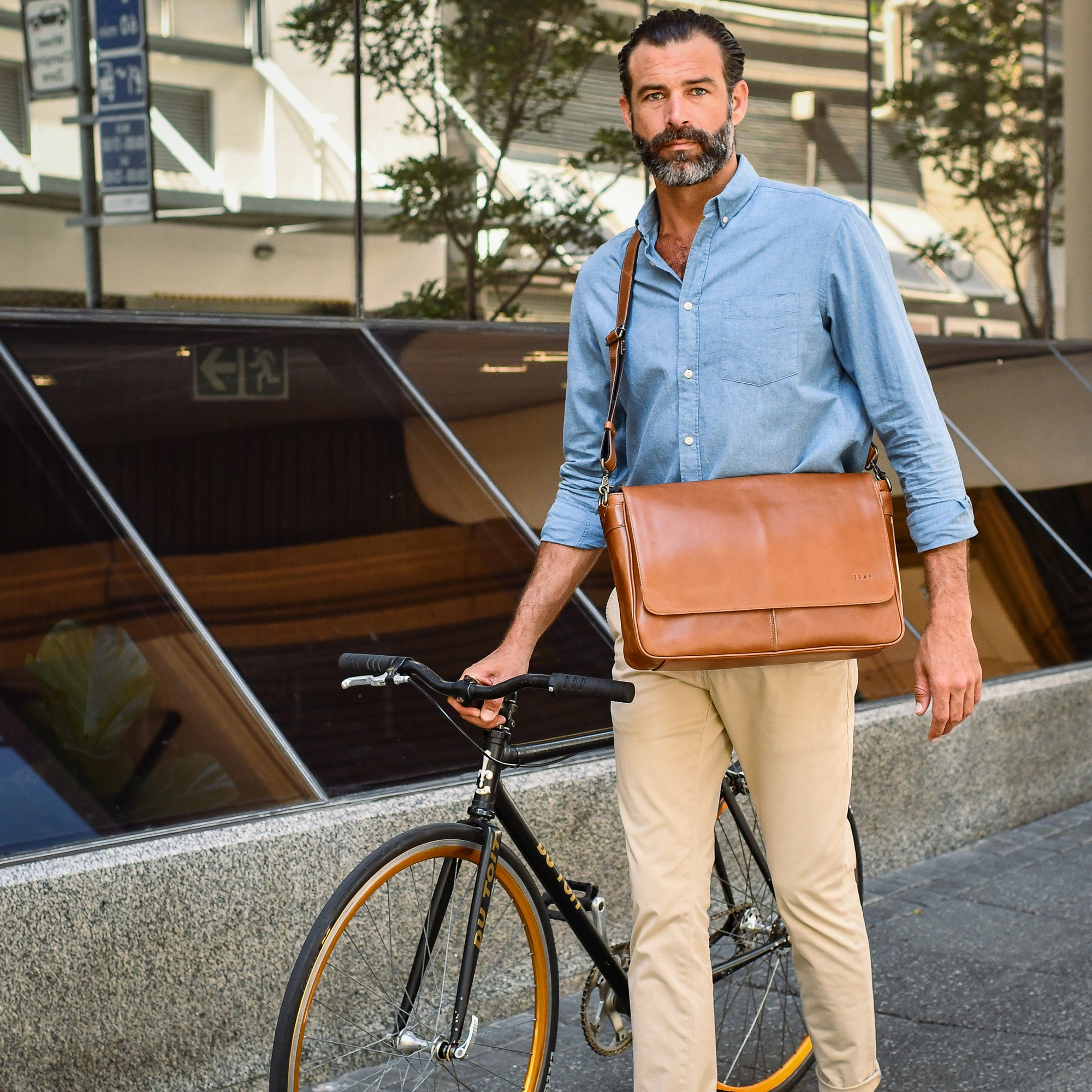Man holding a brown leather bag next to a bicycle in an urban setting