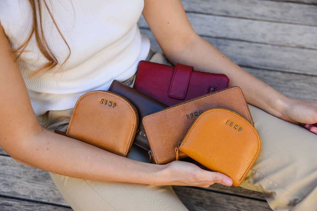 Person holding multiple leather pouches of different colors on a wooden surface
