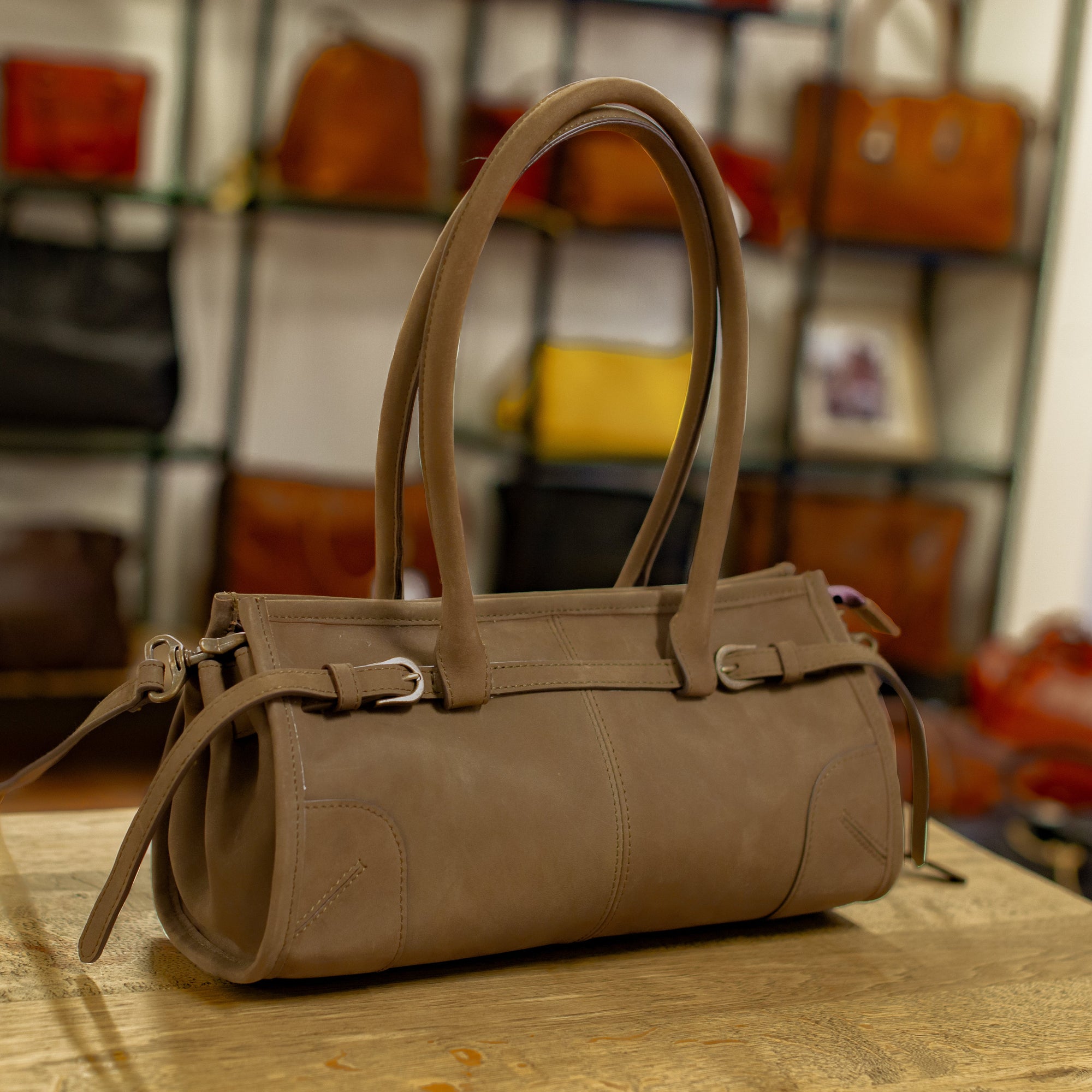 Brown leather handbag on a wooden surface with a blurred background of other bags.
