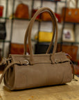 Brown leather handbag on a wooden surface with a blurred background of other bags.