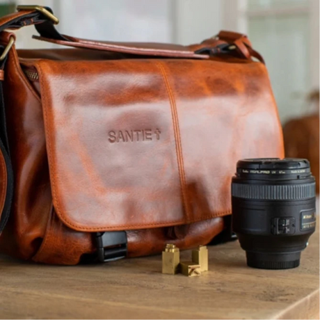 Brown leather camera bag with a camera on a wooden surface