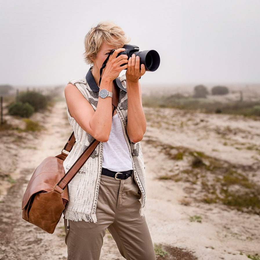 Woman holding a camera to her face, wearing a brown leather camera bag on her hip