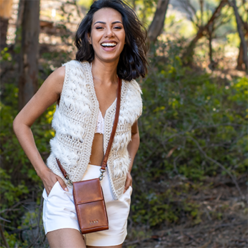 Woman wearing a white crochet vest and white shorts, standing outdoors with greenery in the background.