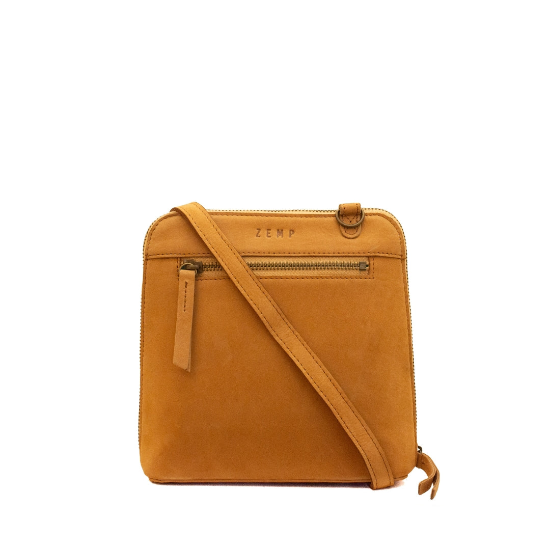 A square-shaped tan suede crossbody bag with a front zippered pocket and a diagonal shoulder strap, shown against a plain white background.