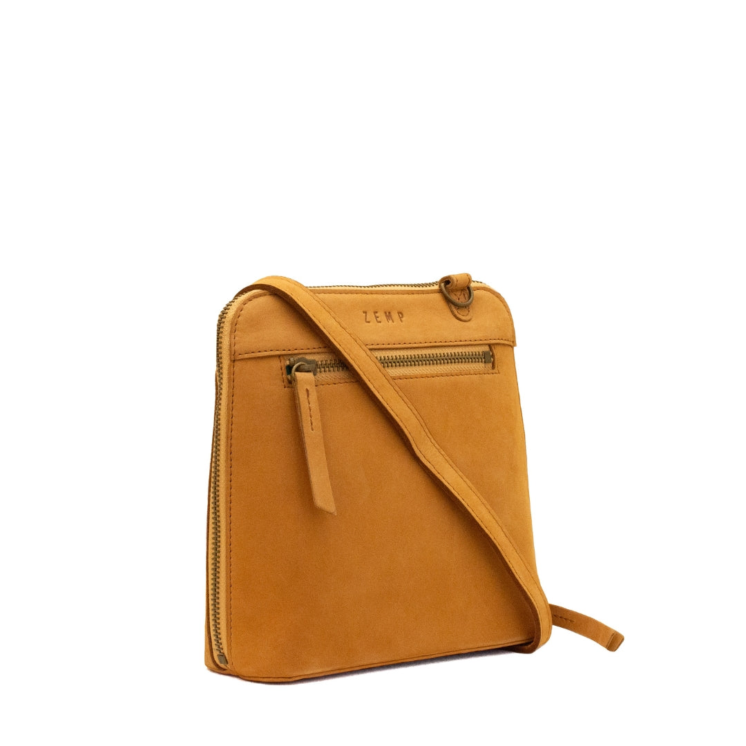A tan suede crossbody bag with a front zippered pocket and a top zipper, featuring the brand name 'ZEMP' embossed on the front, set against a plain white background.