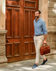 Man holding a brown leather briefcase in front of a large wooden door.