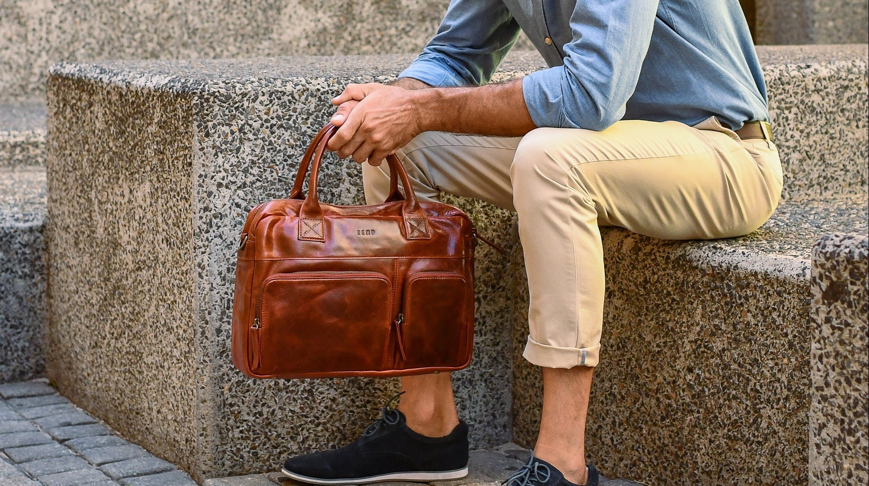 Person holding a brown leather briefcase sitting on stone steps.