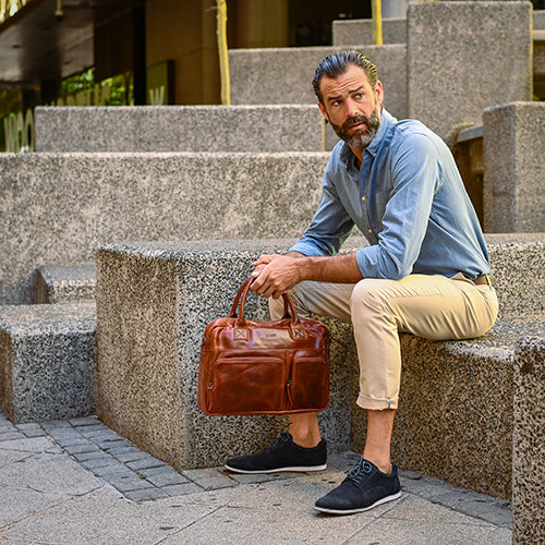 Man sitting on steps holding a brown leather bag in an urban setting