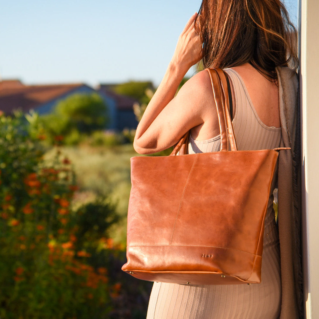 Woman holding a brown leather tote bag with a blurred outdoor background