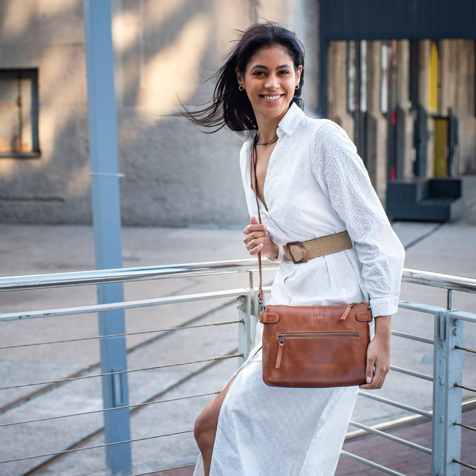 Woman in a white outfit holding a brown leather bag outdoors.