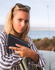 Woman holding a phone with a scenic background of water and mountains.