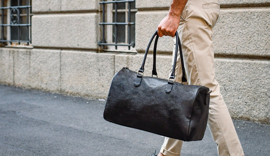 Person walking outdoors holding a black leather bag against a stone building background