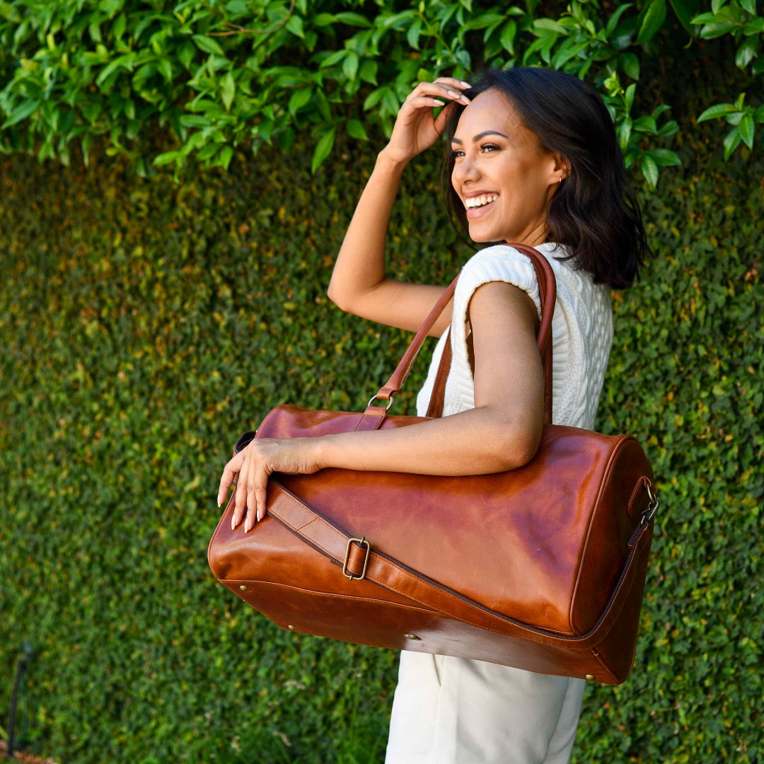 Woman holding a chestnut leather bag against a green leafy background