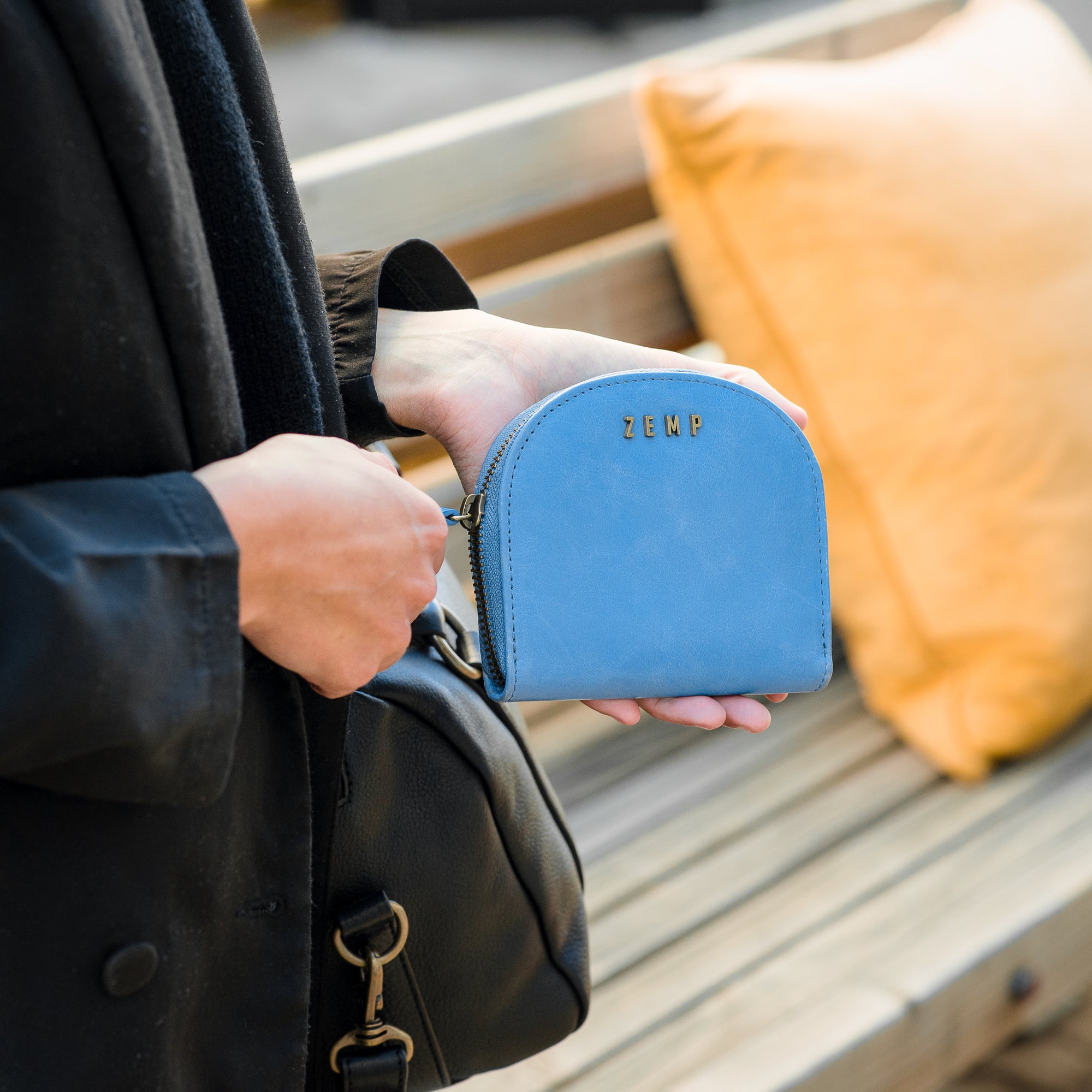 Person holding a blue wallet with 'Zemp' branding on a wooden bench.