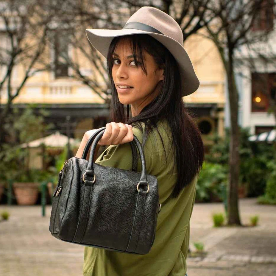 Woman holding a black handbag outdoors with trees and buildings in the background