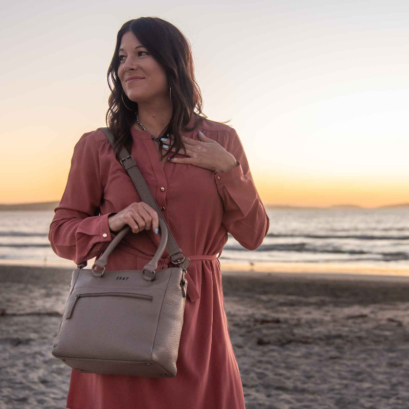 Woman holding a beige handbag on a beach at sunset