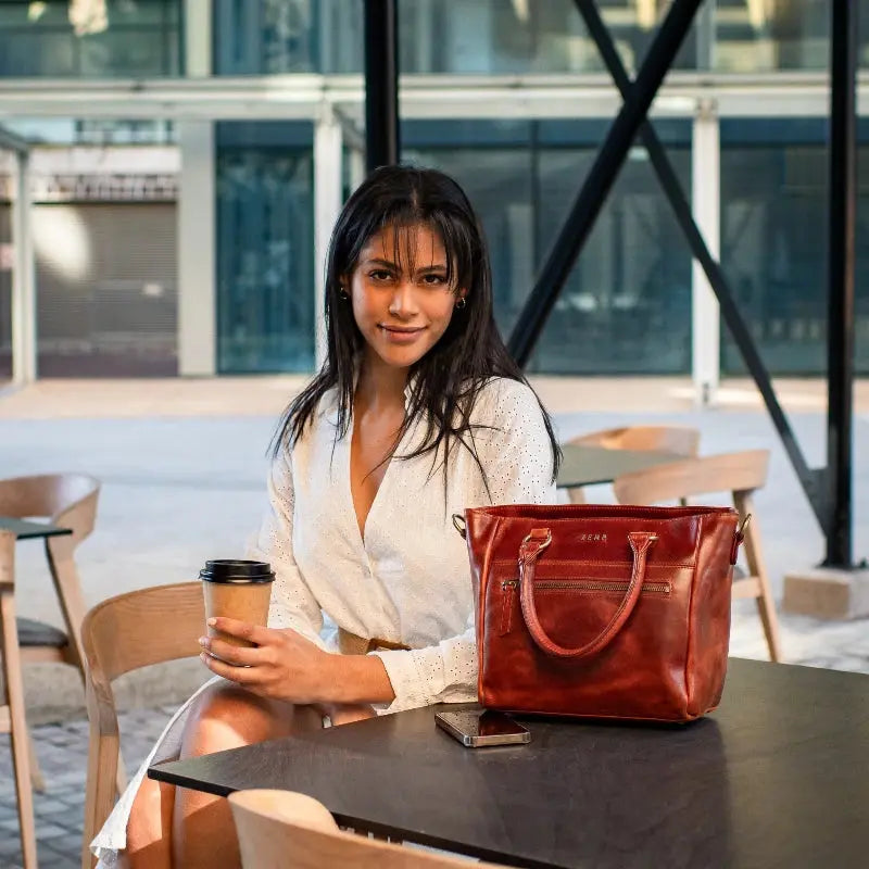 Woman sitting at a table with a red handbag and a coffee cup in an outdoor setting.