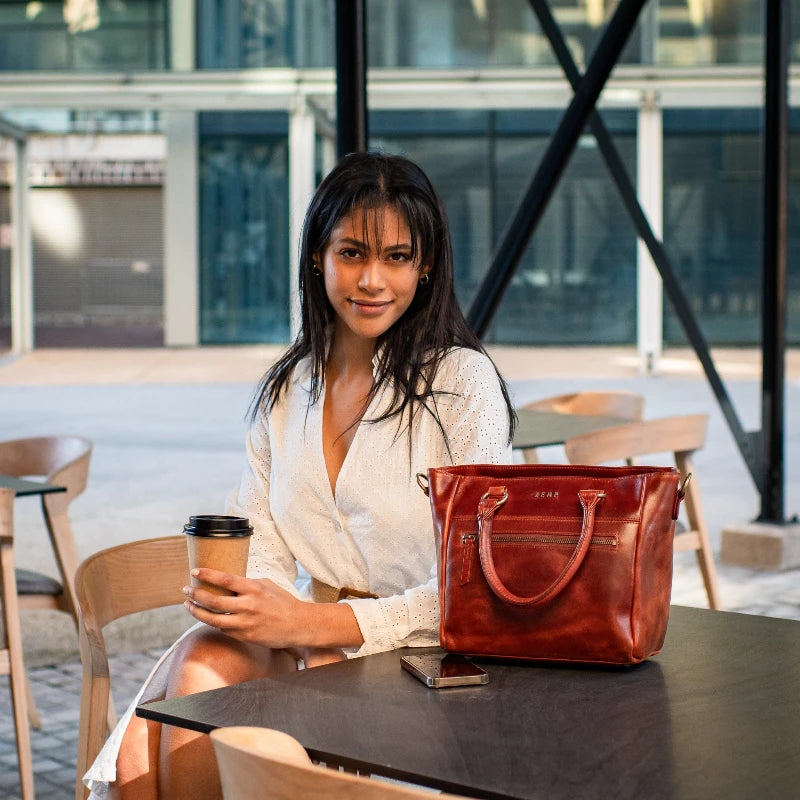 Woman sitting at a table with a red handbag and a coffee cup in an outdoor setting.